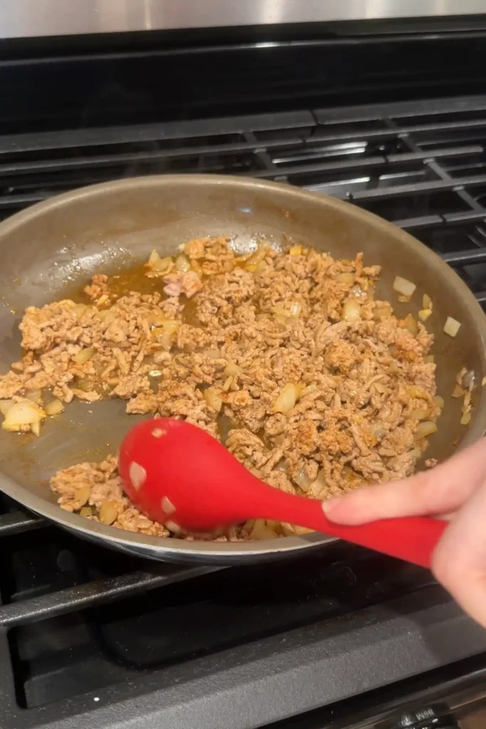Seasoned ground turkey and onions cooking in a skillet for stuffed bell peppers.